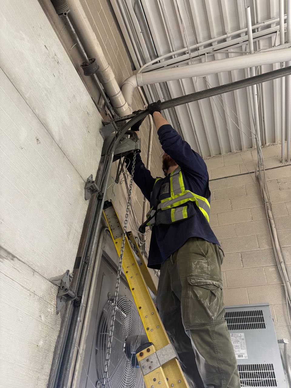 Doorfect technician on a ladder servicing overhead garage door hardware on a spring repair call