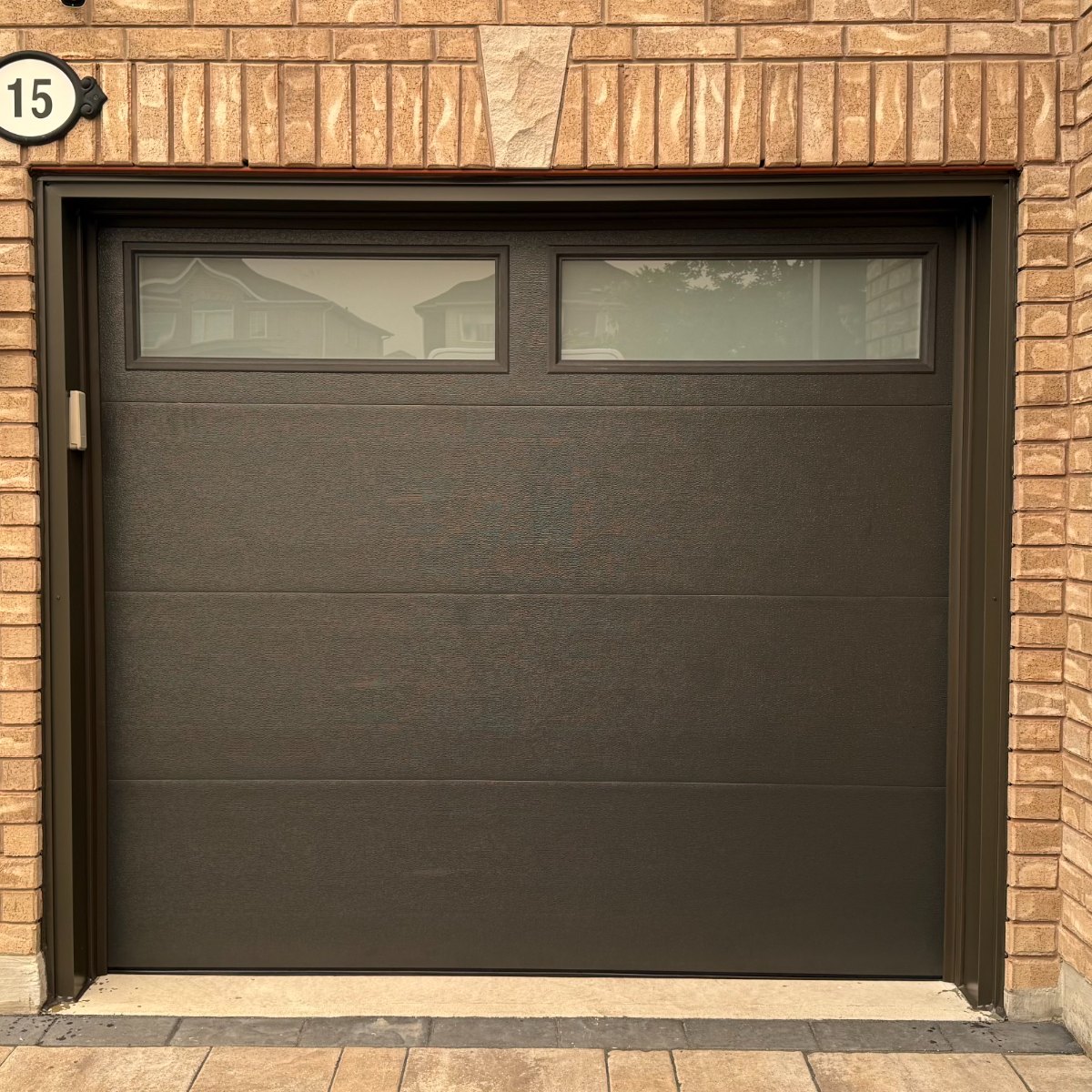 Brown single garage door with window inserts on a brick home
