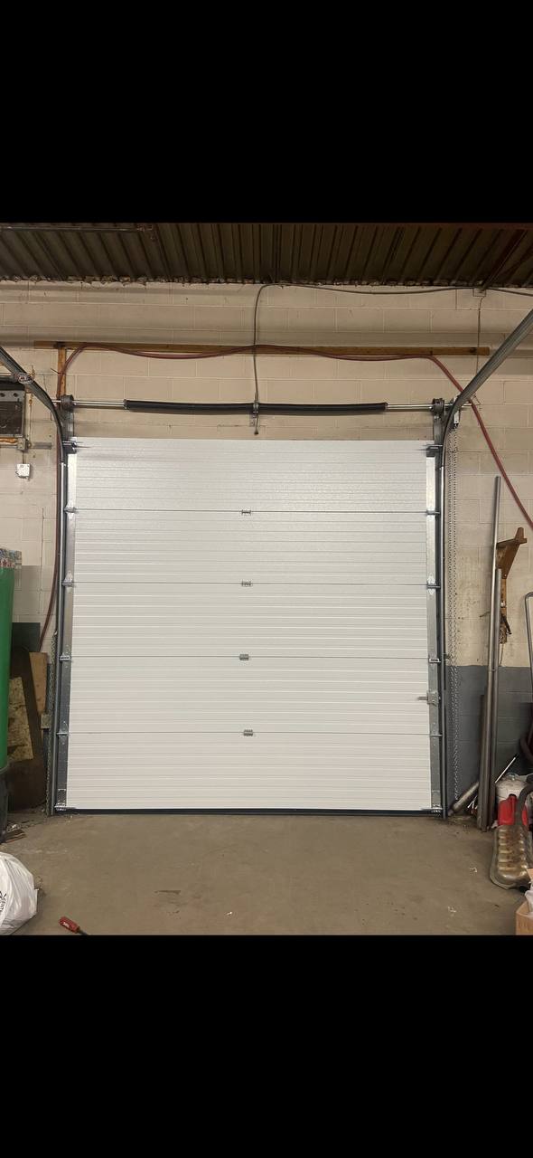 Garage door safety sensor mounted near the bottom of a sectional door for calibration